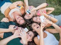 Female Montclair State University students laying in a circle while taking selfies with cellphones.